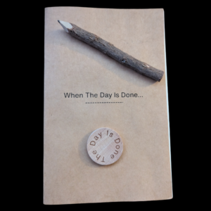 Kraft paper booklet titled “When The Day Is Done…” with a wooden coin and a natural wood pencil placed on top.